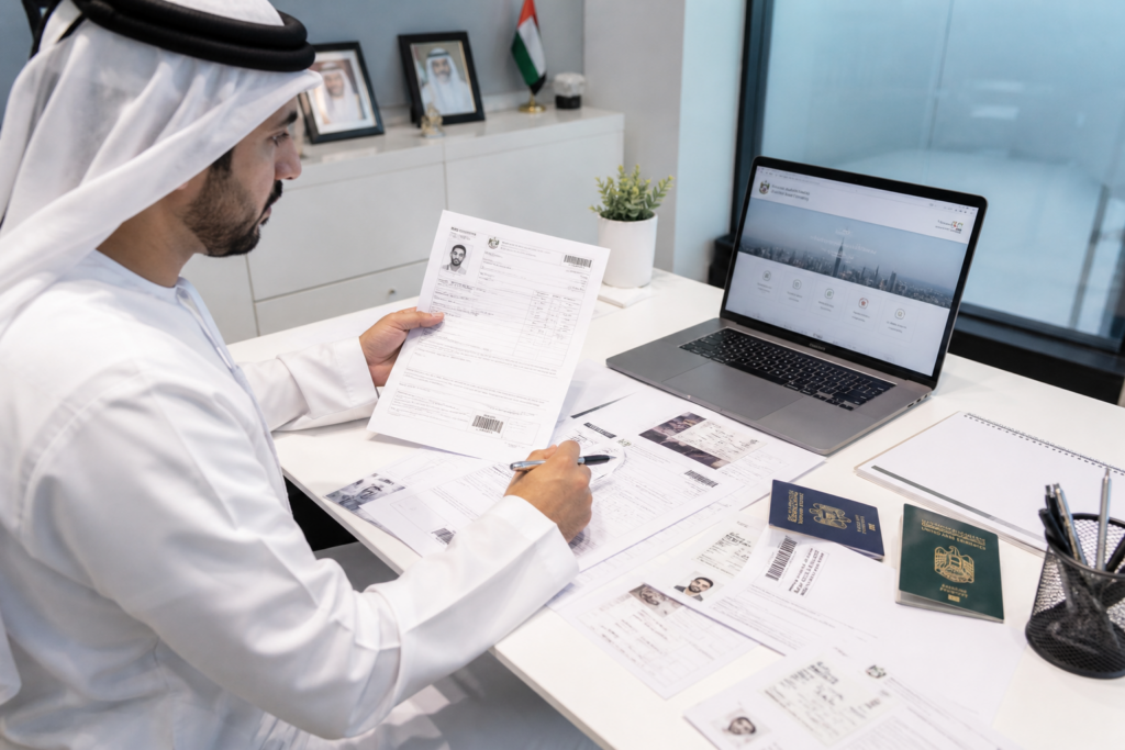 HR manager reviewing UAE visa documents and passports on a white desk with laptop open to government portal
