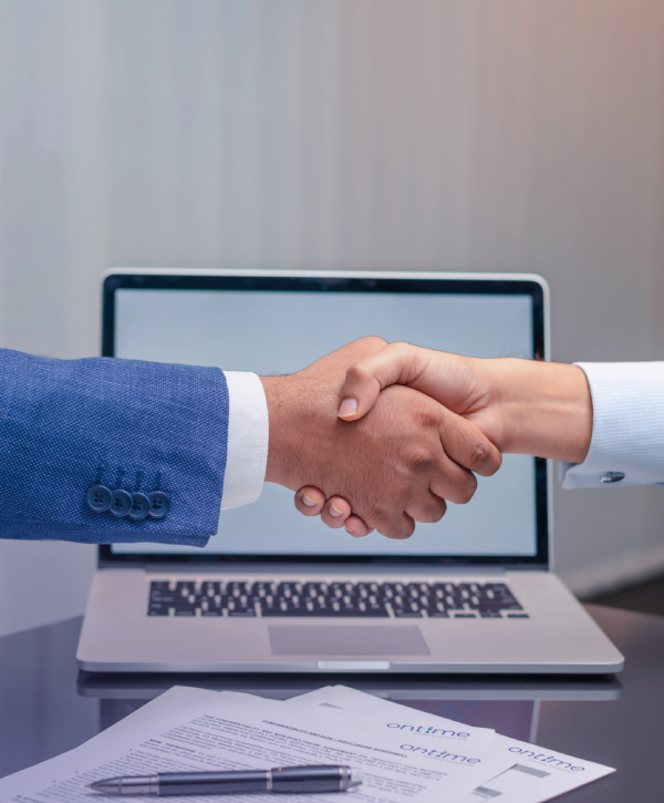 Close-up of a handshake in front of an open laptop, with a pen and signed documents on the desk below. for pro services in uae